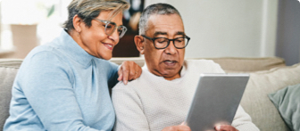 An older woman and an older man sitting on a couch looking at a tablet together.