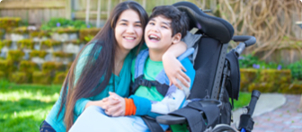 An adult woman with her arm around her young son who is using a wheelchair.